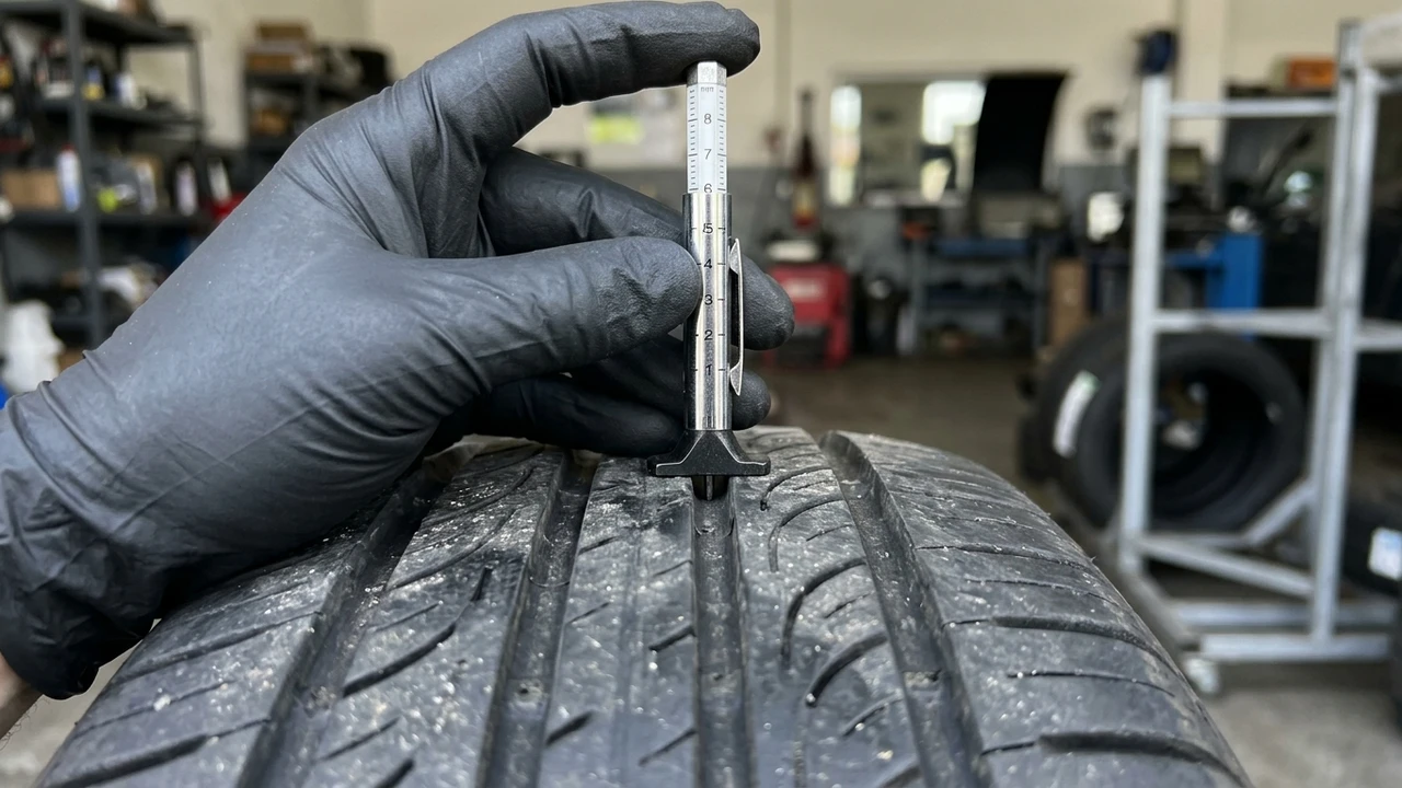 Technician pressing digital color-coded tire tread depth gauge into rubber tread groove of vehicle tire